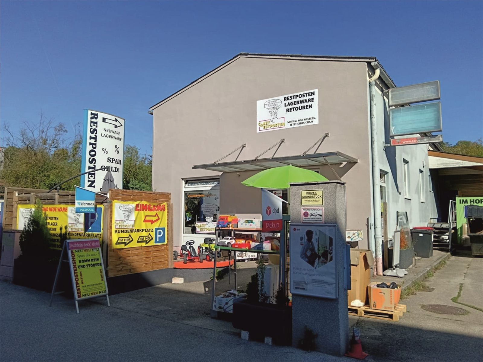 Außenansicht des Crazy Restpostenshop in Amstetten mit Beschilderung, Kundenparkplatz im Hof und Paketshop-Station
